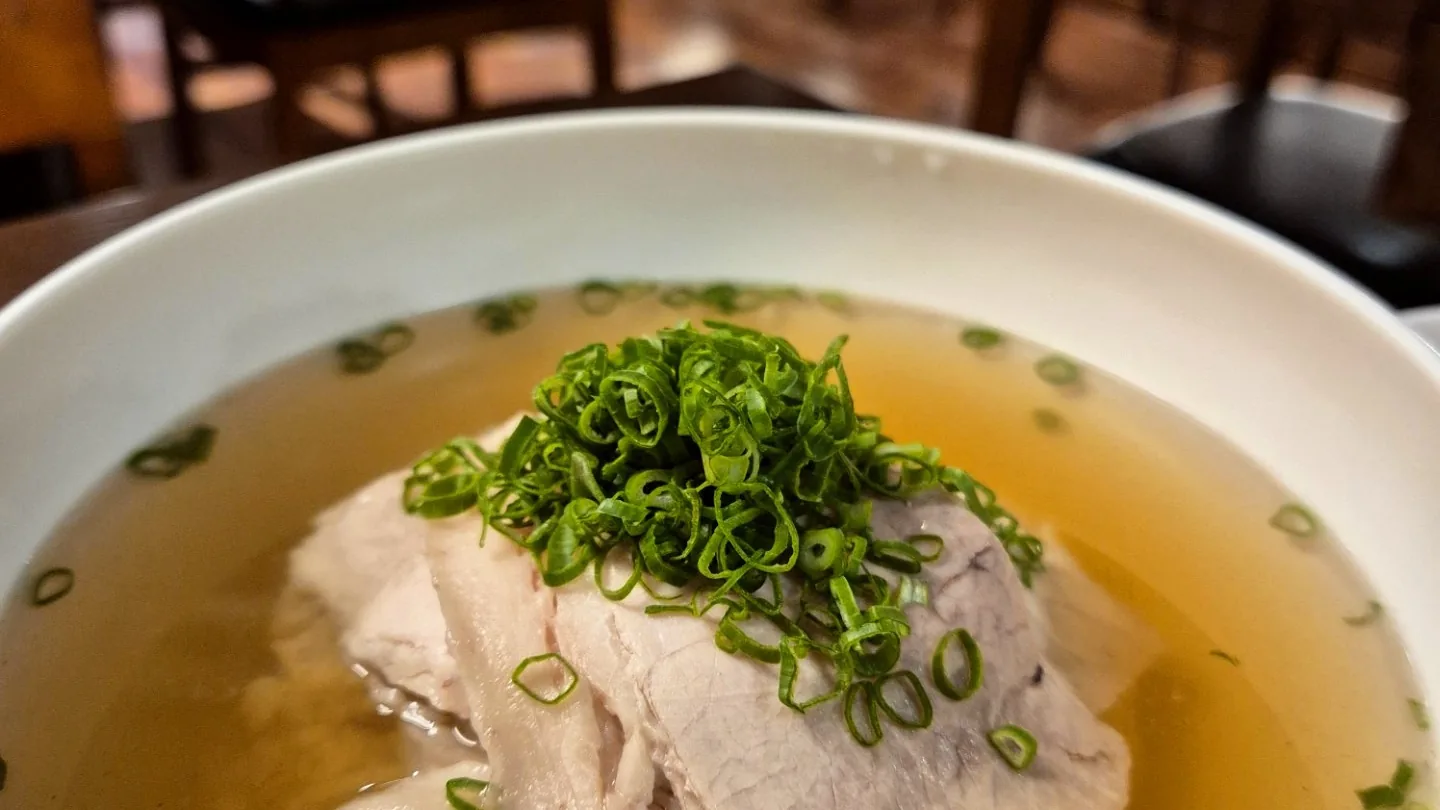 맑은 국물에 고기를 담고 쪽파를 올린 곰탕 한 그릇. 뒤로 한옥 홀의 좌석이 흐리게 보인다.